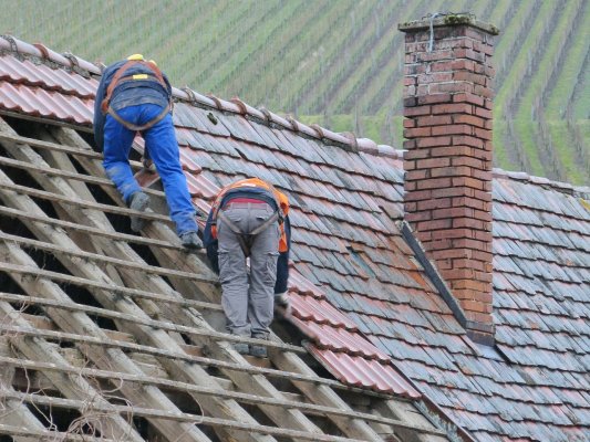 2 people replacing really old tiles on a roof